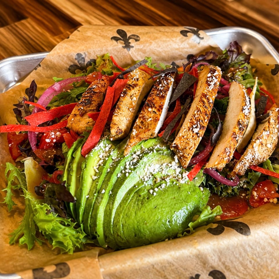 Grilled chicken salad with avocado, red onion, and tortilla strips on parchment paper.
